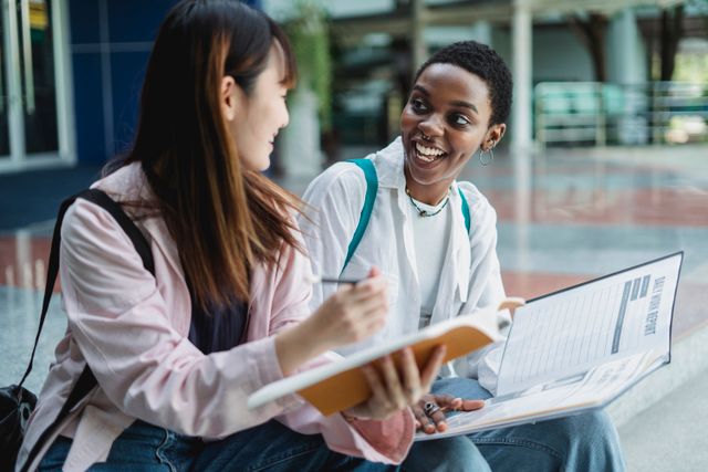Three international students walking together across a university campus, holding folders and smiling